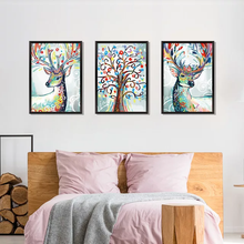Load image into Gallery viewer, A set of three colorful wall decals featuring abstract representations of deer and trees in a bedroom setting.