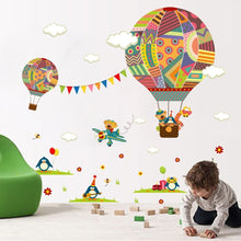 Load image into Gallery viewer, Colorful wall decal featuring various cartoonish air balloons and accompanying imagery such as a hot air balloon, applied on a wall behind a green chair with a child standing in front.