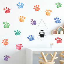 Load image into Gallery viewer, Colorful paw print-shaped wall decals arranged in a pattern on a white wall, with a small decorative owl figure in the foreground.